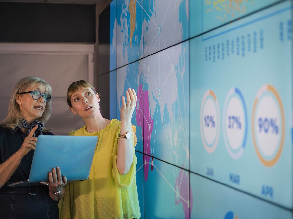 Professionals review data on a laptop and on a larger wall display